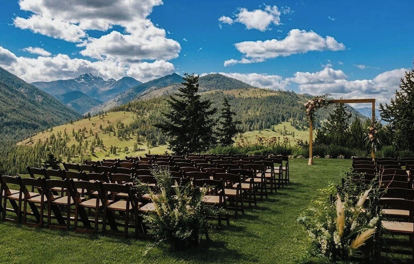 An outdoor seating area with rows of wooden chairs and tables, set against a backdrop of mountains and a clear sky.