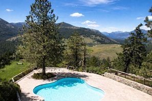 A swimming pool with a mountain view, surrounded by trees and a stone wall. - Sun Mountain Lodge (Winthrop)