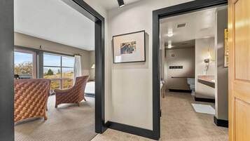 A hotel room with a large window, a framed picture on the wall, and a wicker chair.