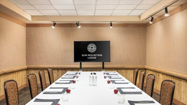 A conference room with a long table, chairs, a television screen, and a logo for Sun Mountain Lodge. - Sun Mountain Lodge (Winthrop)