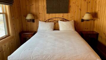 Una habitación con cama, dos mesitas de noche, dos lámparas de pared y un ventanal con persianas.