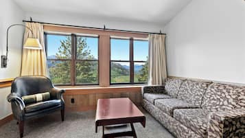 A room with a large window, a leather armchair, a patterned sofa, and a small table.
