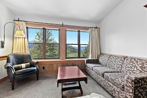 A room with a large window, a leather armchair, a patterned sofa, and a small table. - Sun Mountain Lodge (Winthrop)