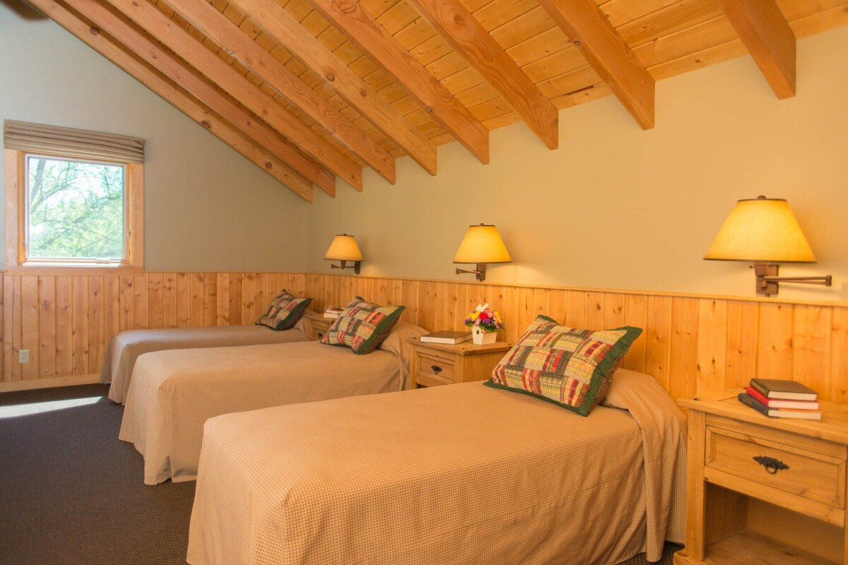 A room with two beds, wooden walls, a sloped ceiling, and wall-mounted lamps.