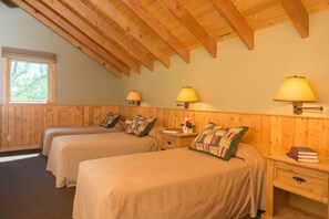 Una habitación con dos camas, paredes de madera, techo inclinado y lámparas fijadas a la pared.