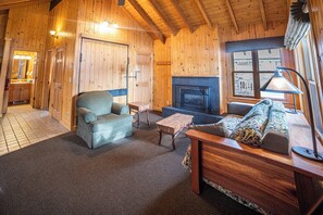 A wooden interior with a sofa, armchair, fireplace, and a small table.