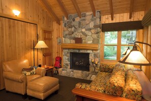 A cozy room with a stone fireplace, a leather armchair, a patterned sofa, and a lamp.