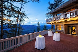 Une terrasse en bois avec des tables rondes, des guirlandes lumineuses et une vue sur les montagnes.