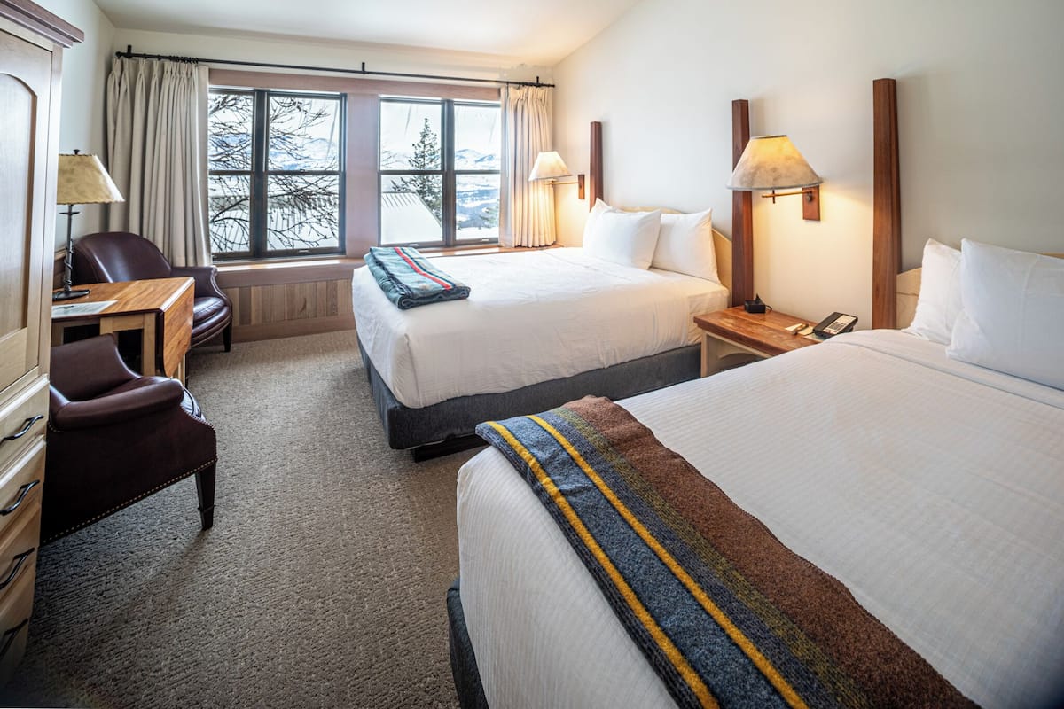 A hotel room with two beds, a desk, a chair, and a window with curtains.