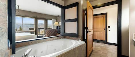 A modern bathroom with a large bathtub, a mirror, and a view of a balcony.