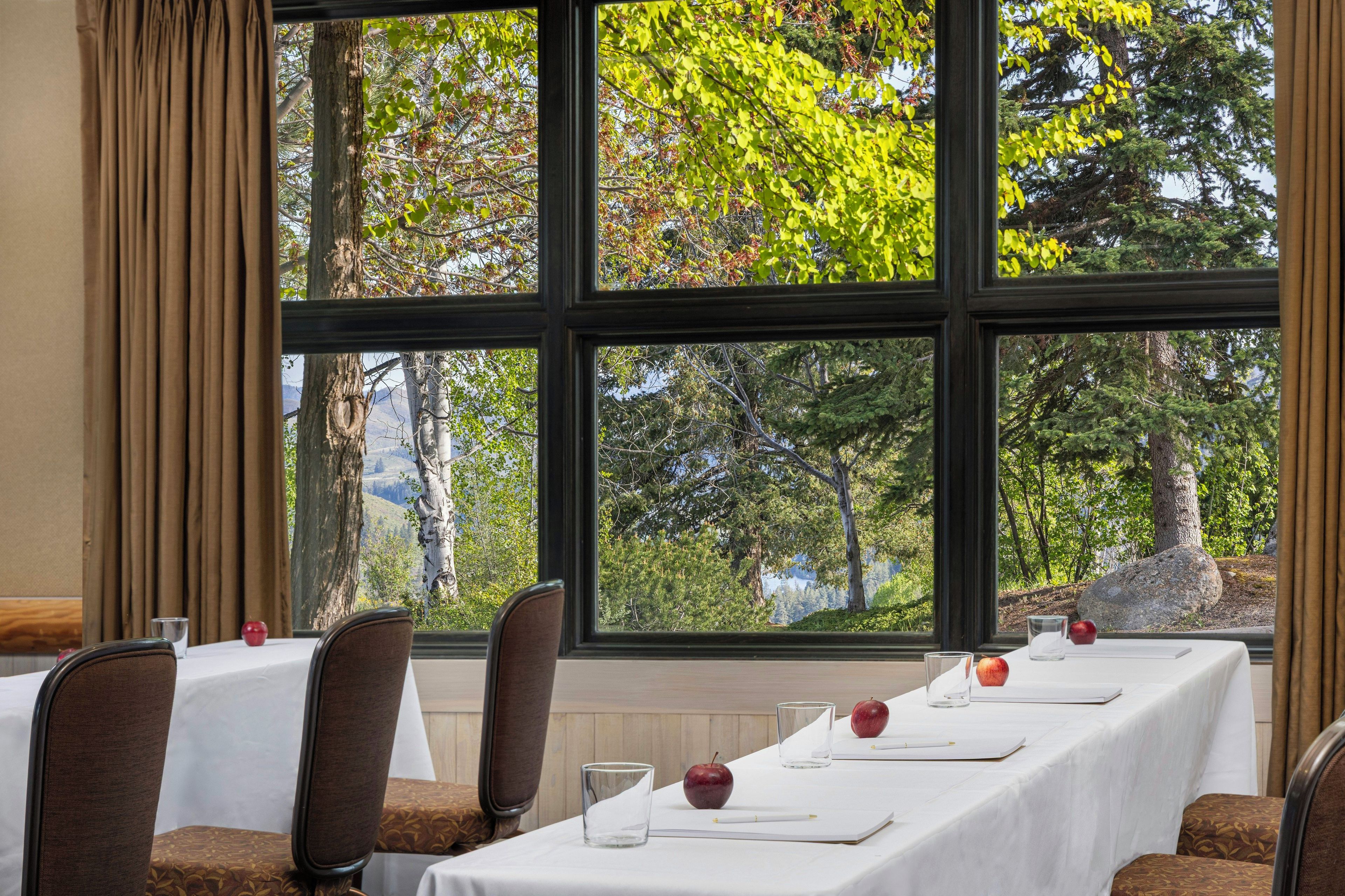 Comedor con una mesa dispuesta para seis, sillas y vistas a árboles a través de amplios ventanales.