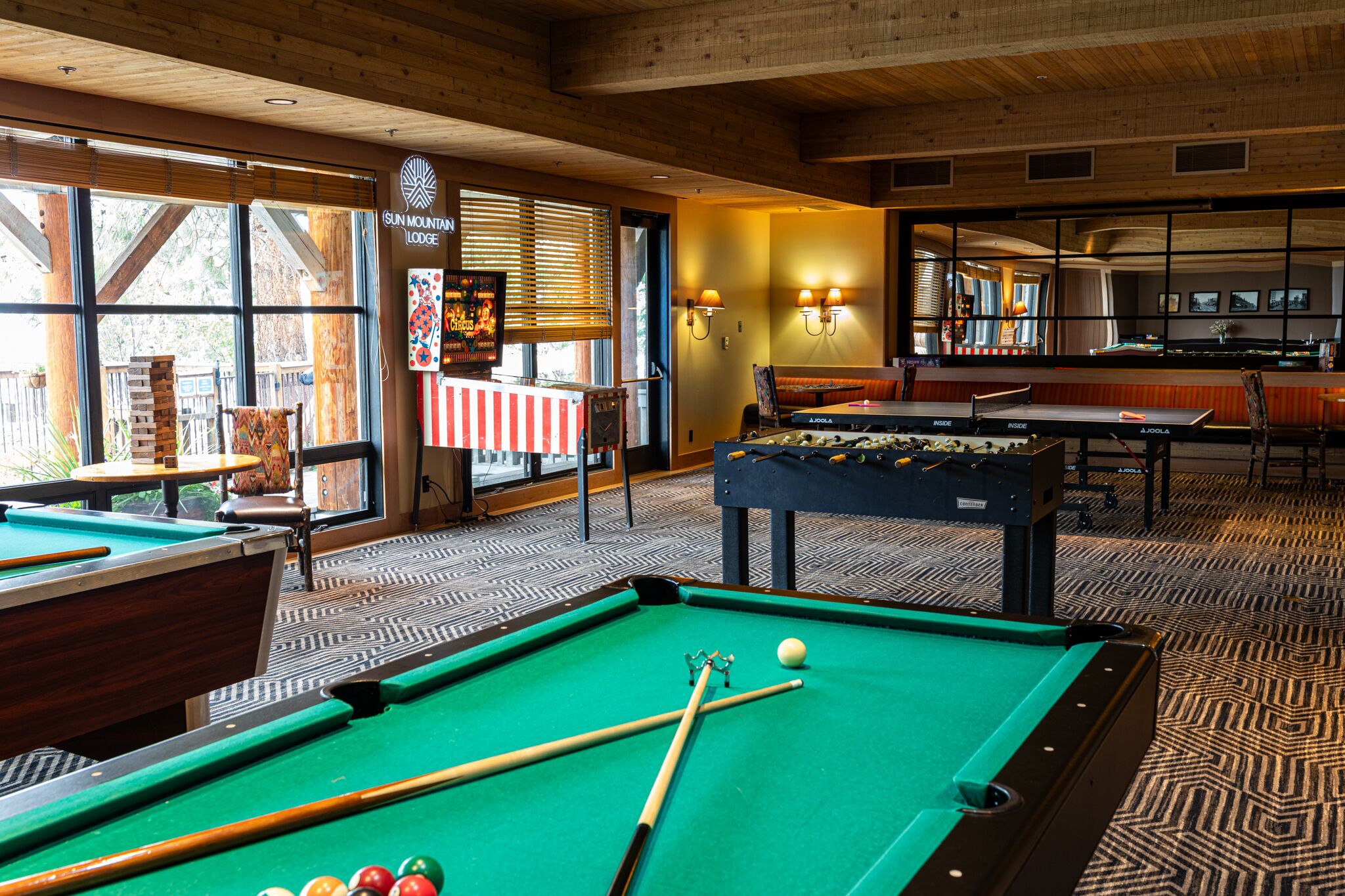 A pool table with a billiard cue and balls, a pool table in the background, and a sign for Sun Mountain Lodge.
