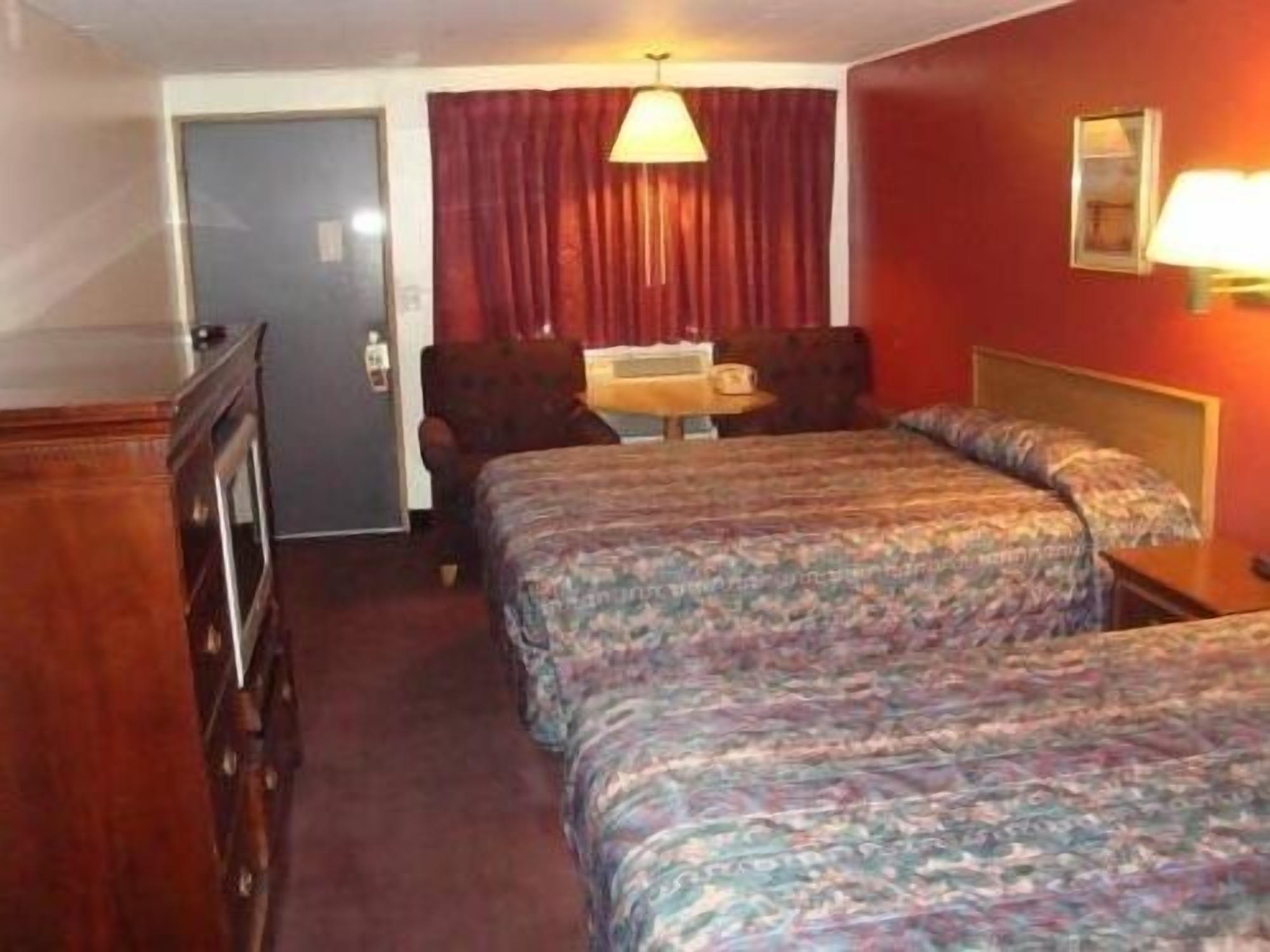 Une chambre d’hôtel avec deux lits, un bureau, une chaise, une lampe et une armoire.