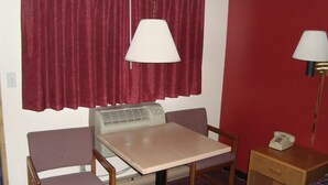 A compact room with a desk, two chairs, a lamp, a telephone, and a bed with a patterned blanket. - Willow Springs Motel (Cheney)