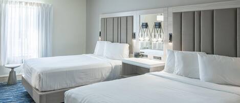 Ein Hotelzimmer mit zwei Betten, einem Nachttisch, einem Spiegel und einem Fenster mit Vorhängen.