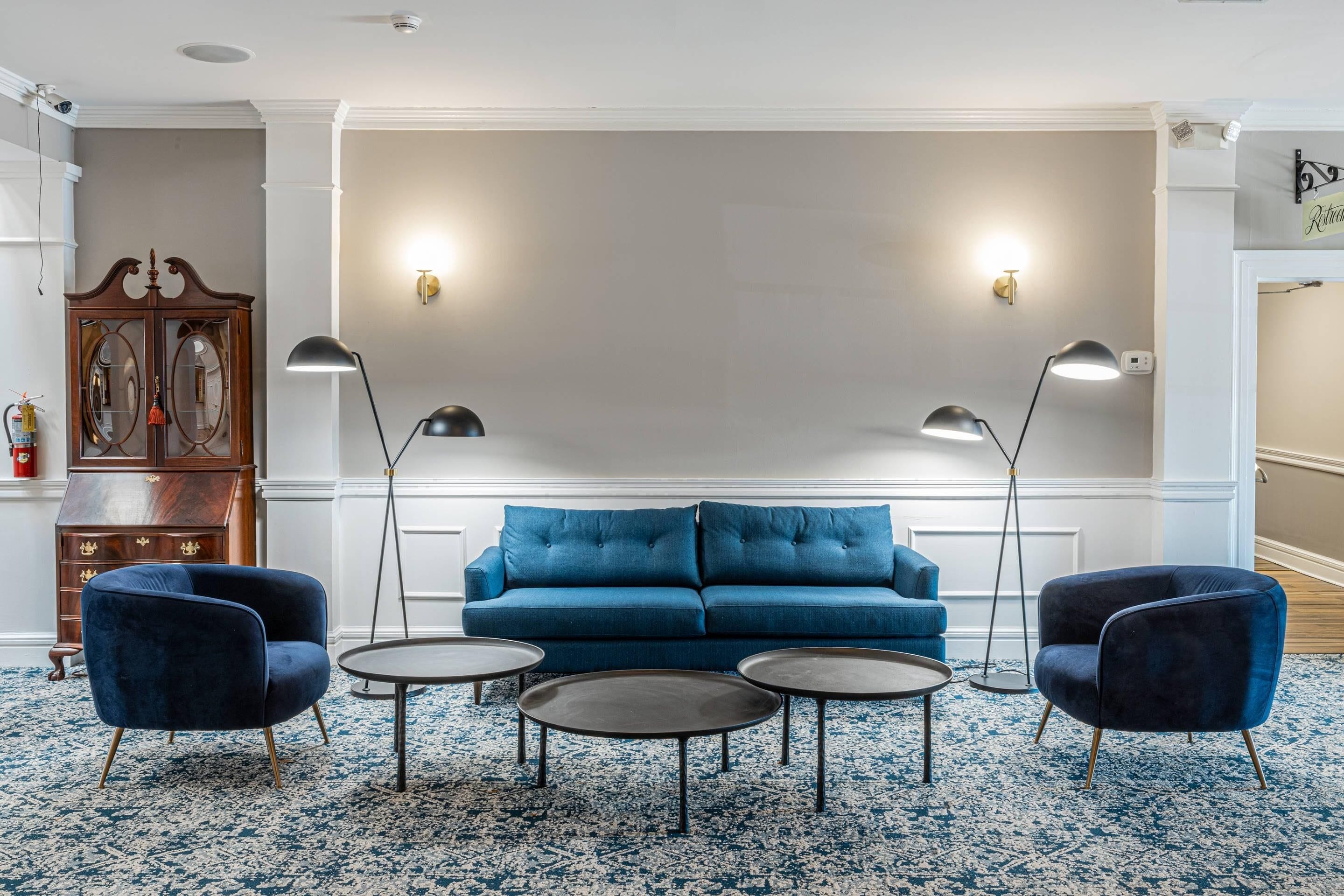 Una sala de estar moderna con un sofá azul, dos sillones y tres mesas redondas.