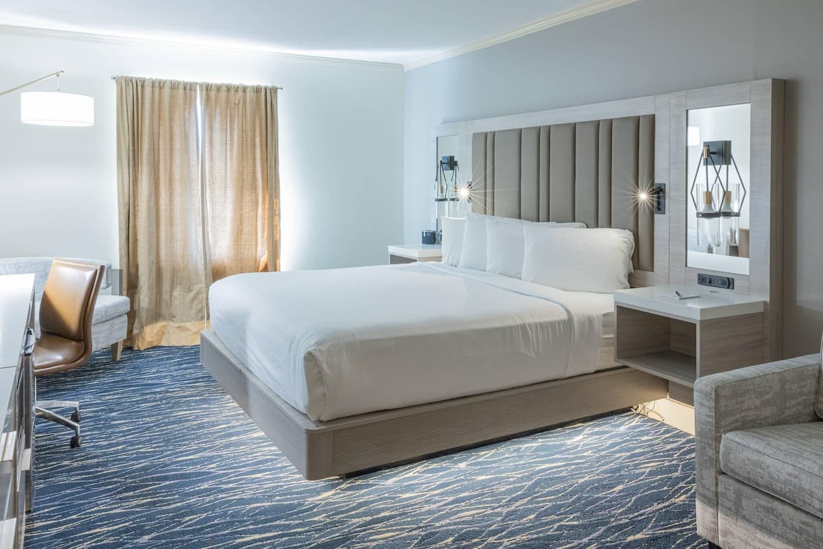 A hotel room with a large bed, a desk, a chair, a nightstand, and a mirror.
