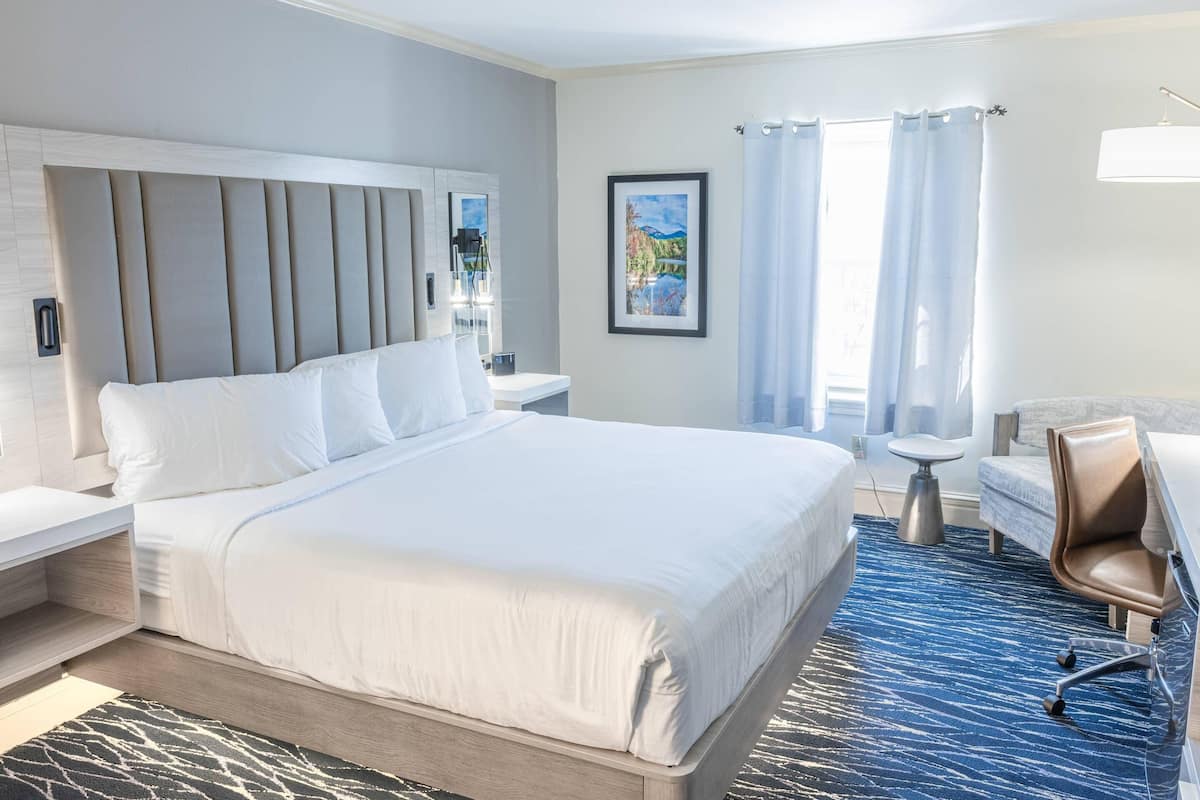 A modern hotel room with a large bed, a desk, a chair, and a small table.