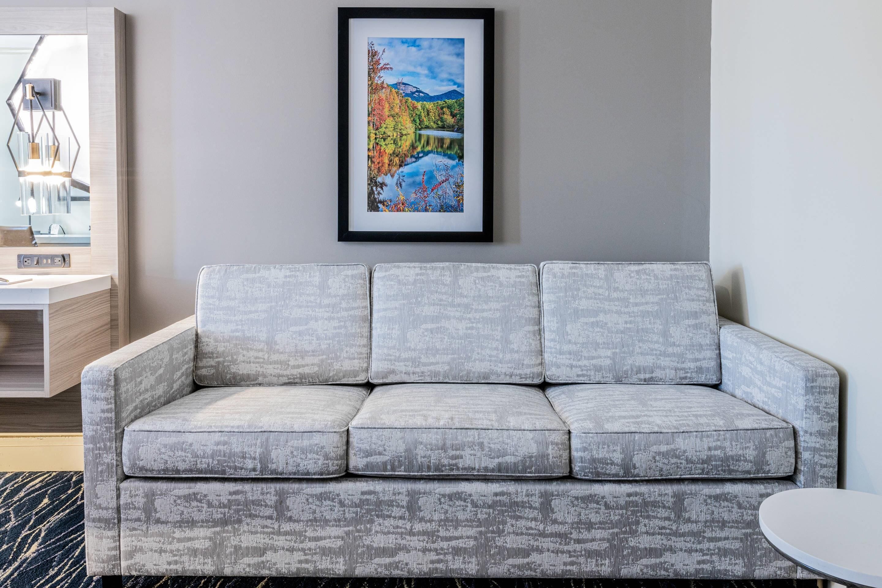 A grey upholstered sofa with a framed landscape painting above it.