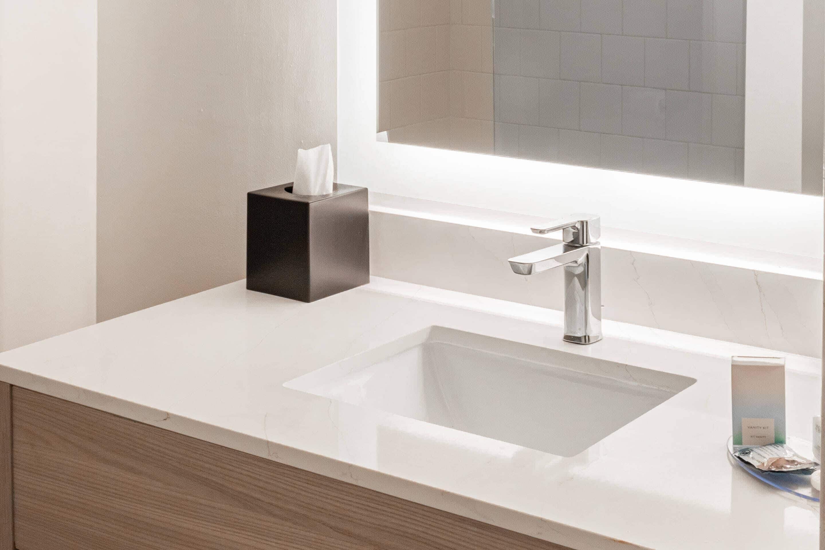 A modern bathroom with a white sink, a black soap dispenser, and a mirror above the sink.