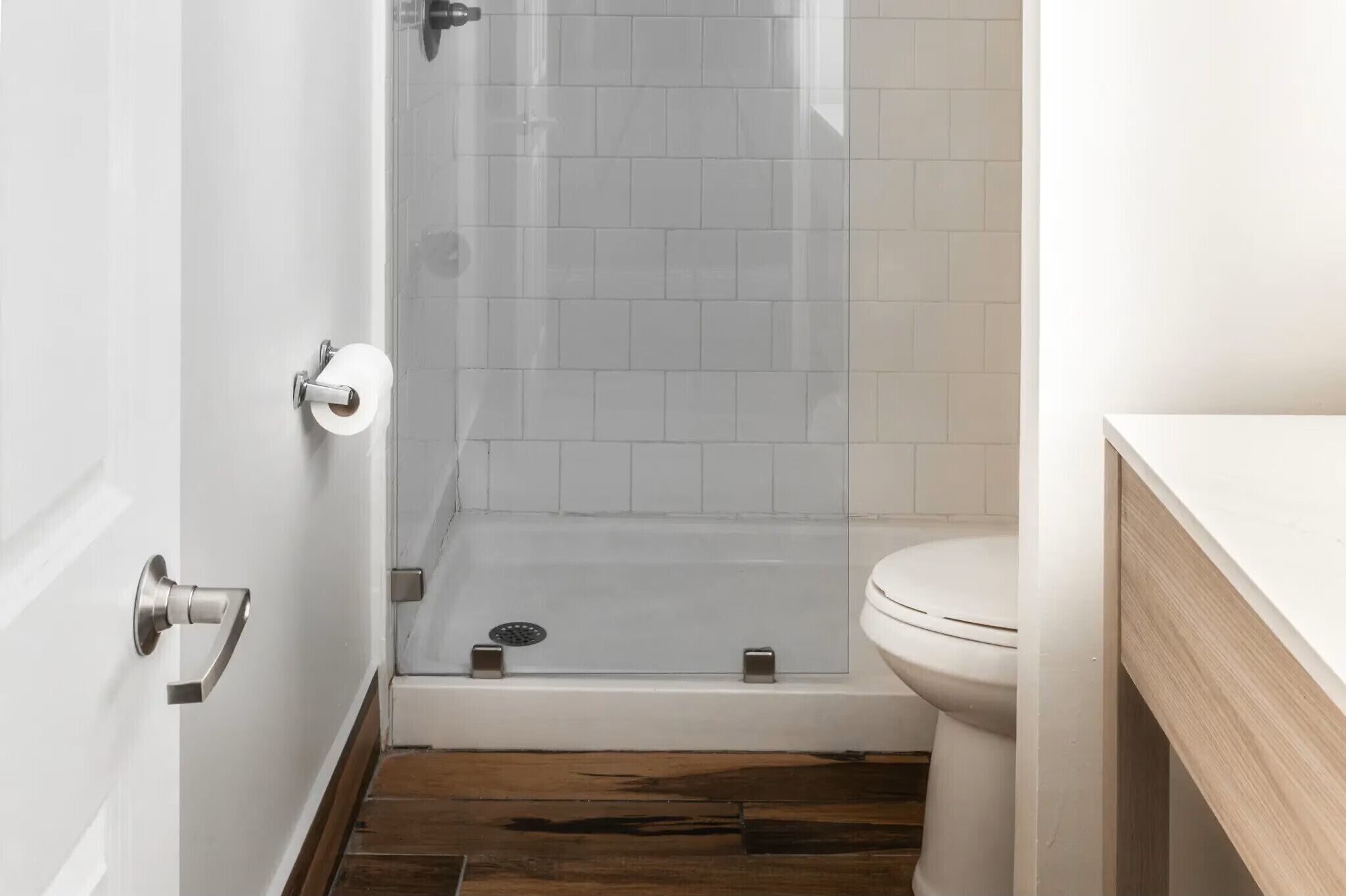 A bathroom with a glass shower enclosure, a toilet, and a wooden floor.