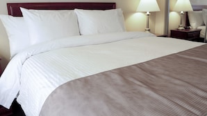 Una cama bien hecha con ropa blanca y beige, dos lámparas de noche y un cabecero de madera.