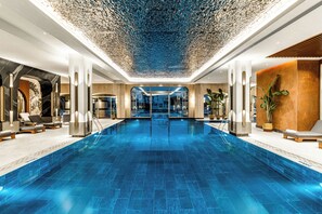 A large indoor swimming pool with a modern design, surrounded by lounge areas and a decorative ceiling. - Kempinski Hotel The Dome Belek - All Inclusive (Serik)