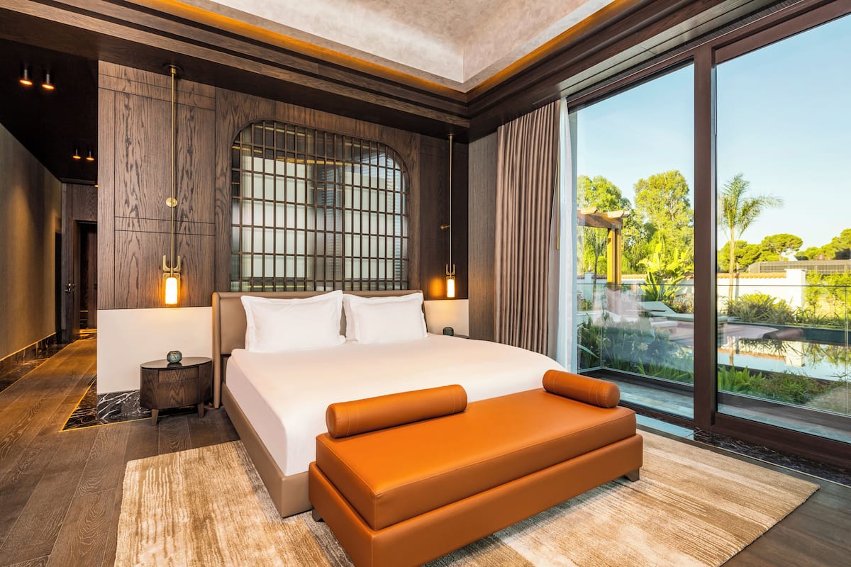 A modern hotel room with a large bed, a view of the outdoors, and a large window.
