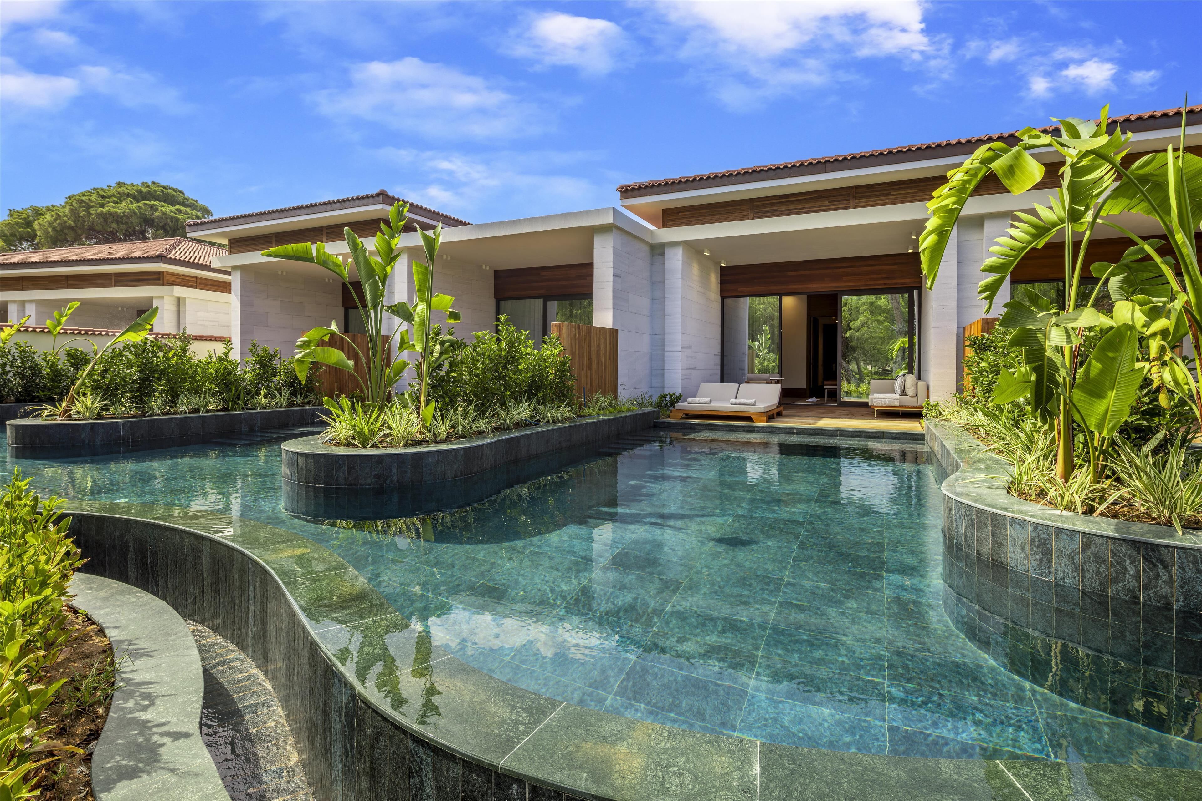 Ein modernes Resort mit klarem Pool, üppigem Grün und einem zweistöckigen Gebäude mit großen Fenstern.