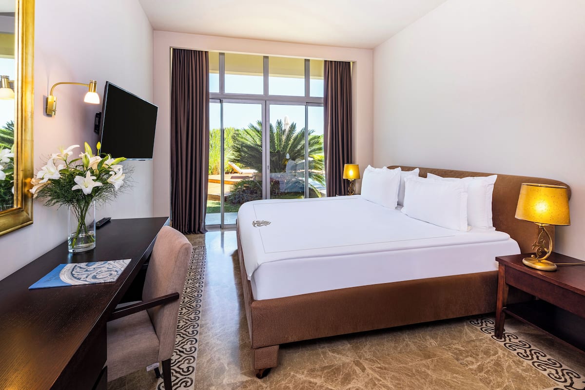 A hotel room with a bed, a desk, a chair, a TV, and a window with curtains.