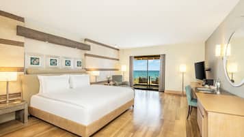Quarto de hotel com uma cama grande, escrivaninha, cadeira, televisão e varanda com vista para o mar.