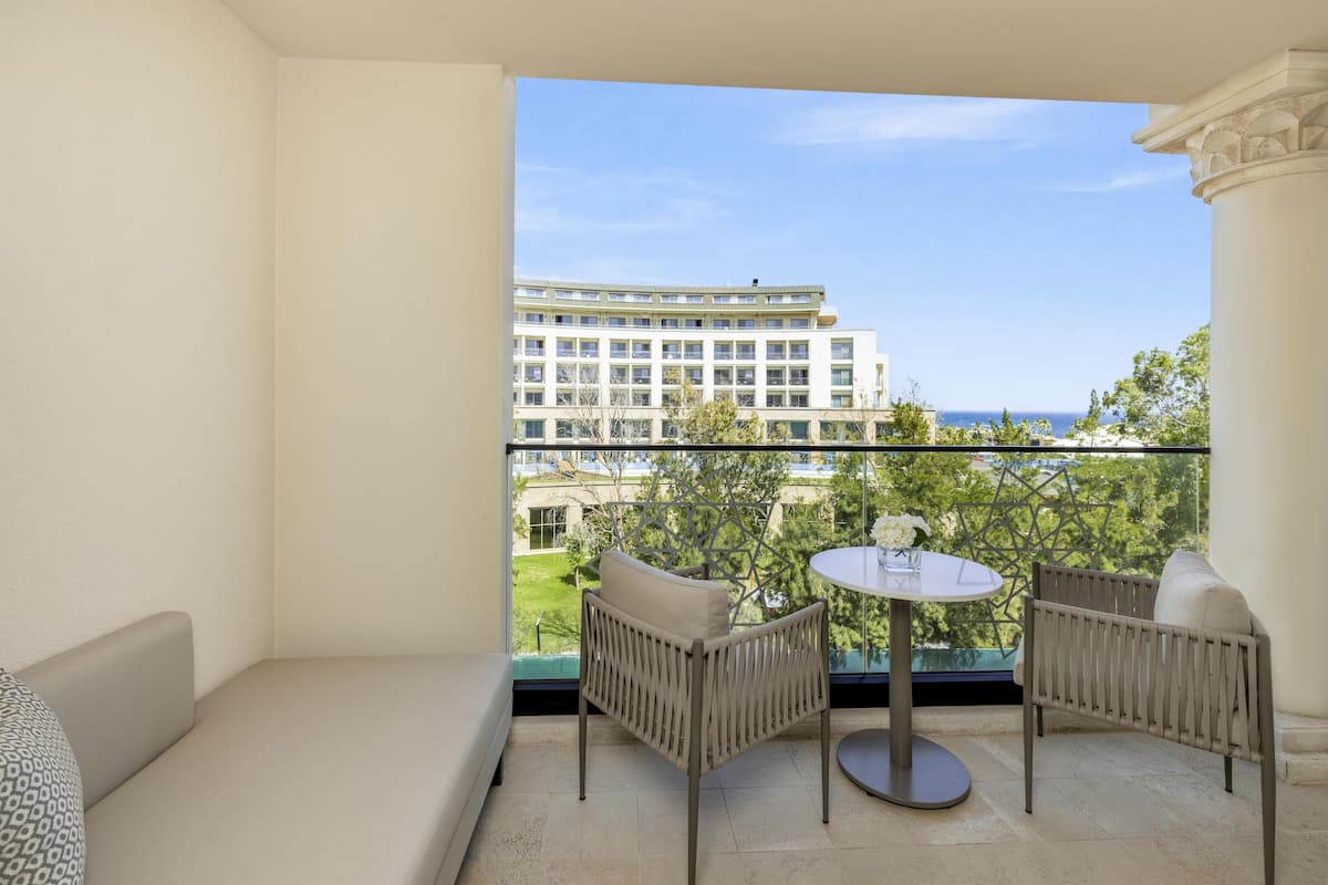 A balcony with a sofa and two chairs, a round table with a vase, and a view of a building and trees.