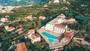 Vue aérienne d’un complexe hôtelier doté d’une grande piscine, de plusieurs bâtiments et d’une végétation luxuriante.