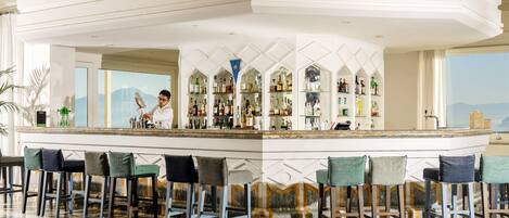 A bar area with a high bar counter, multiple shelves of bottles, and bar stools.