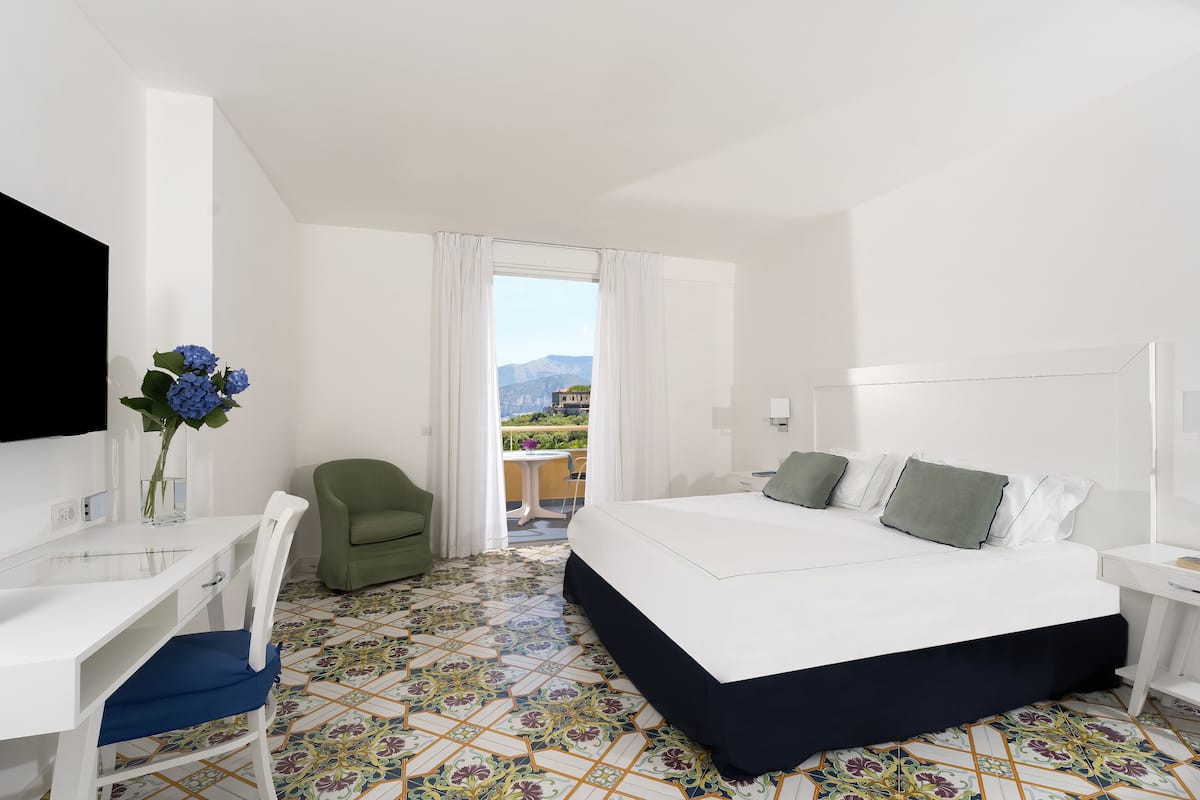 Habitación de hotel con cama, escritorio, silla, televisor y vista al exterior.