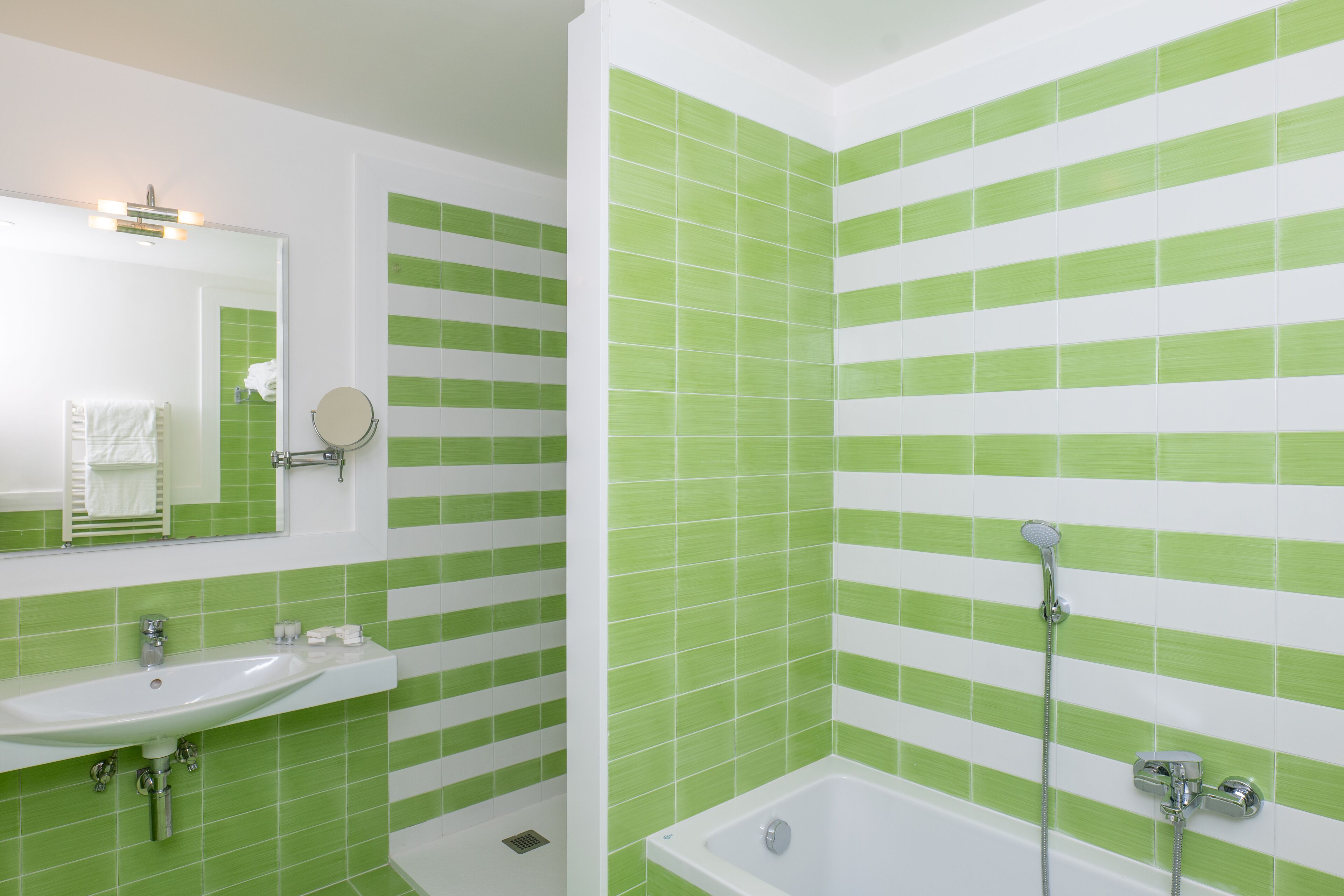 A bathroom with green and white striped tiles, a sink, a mirror, and a bathtub with a showerhead.