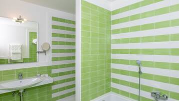 Un baño con baldosas verde y blanco a rayas, un lavabo, un espejo y una bañera con cabezal de ducha.