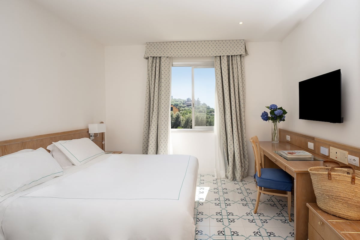 Habitación de hotel con cama, escritorio, silla, televisión y ventana con cortinas.