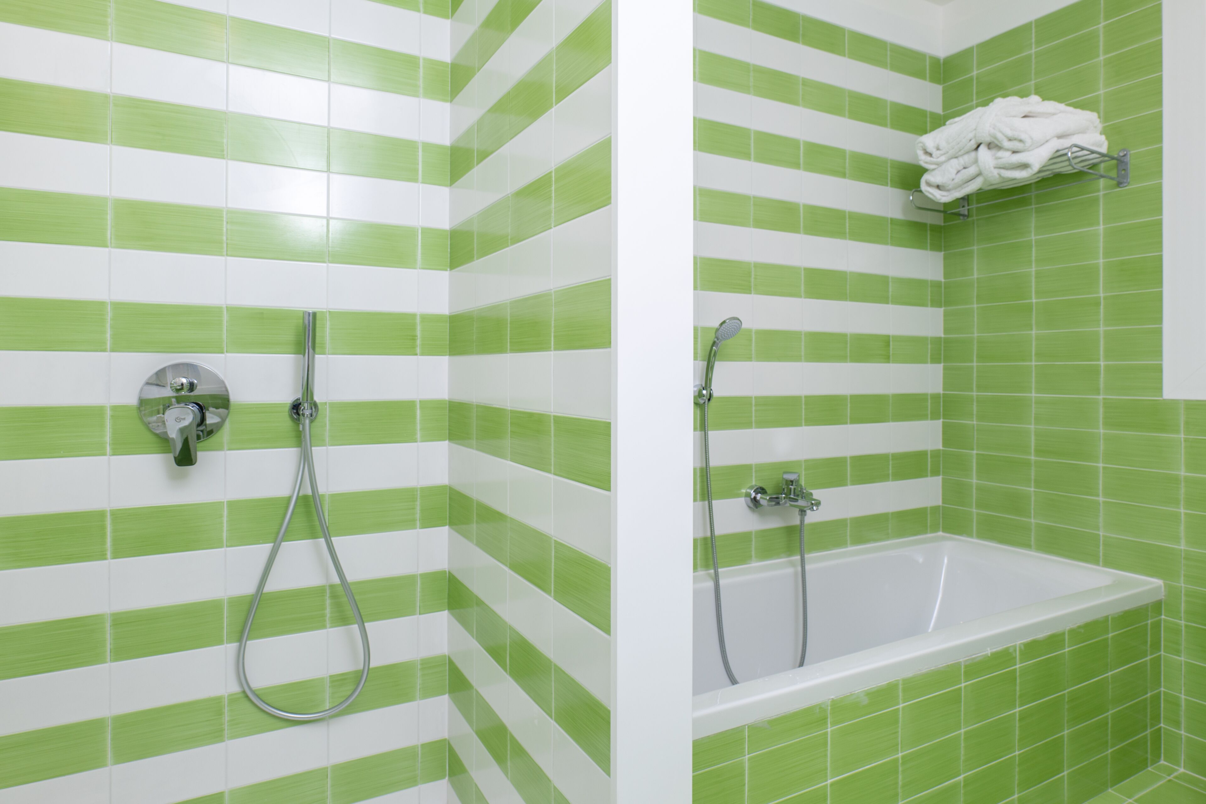 Un baño con baldosas verde y blanco a rayas, una bañera y una ducha con toallero.