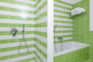 Un baño con baldosas verde y blanco a rayas, una bañera y una ducha con toallero.