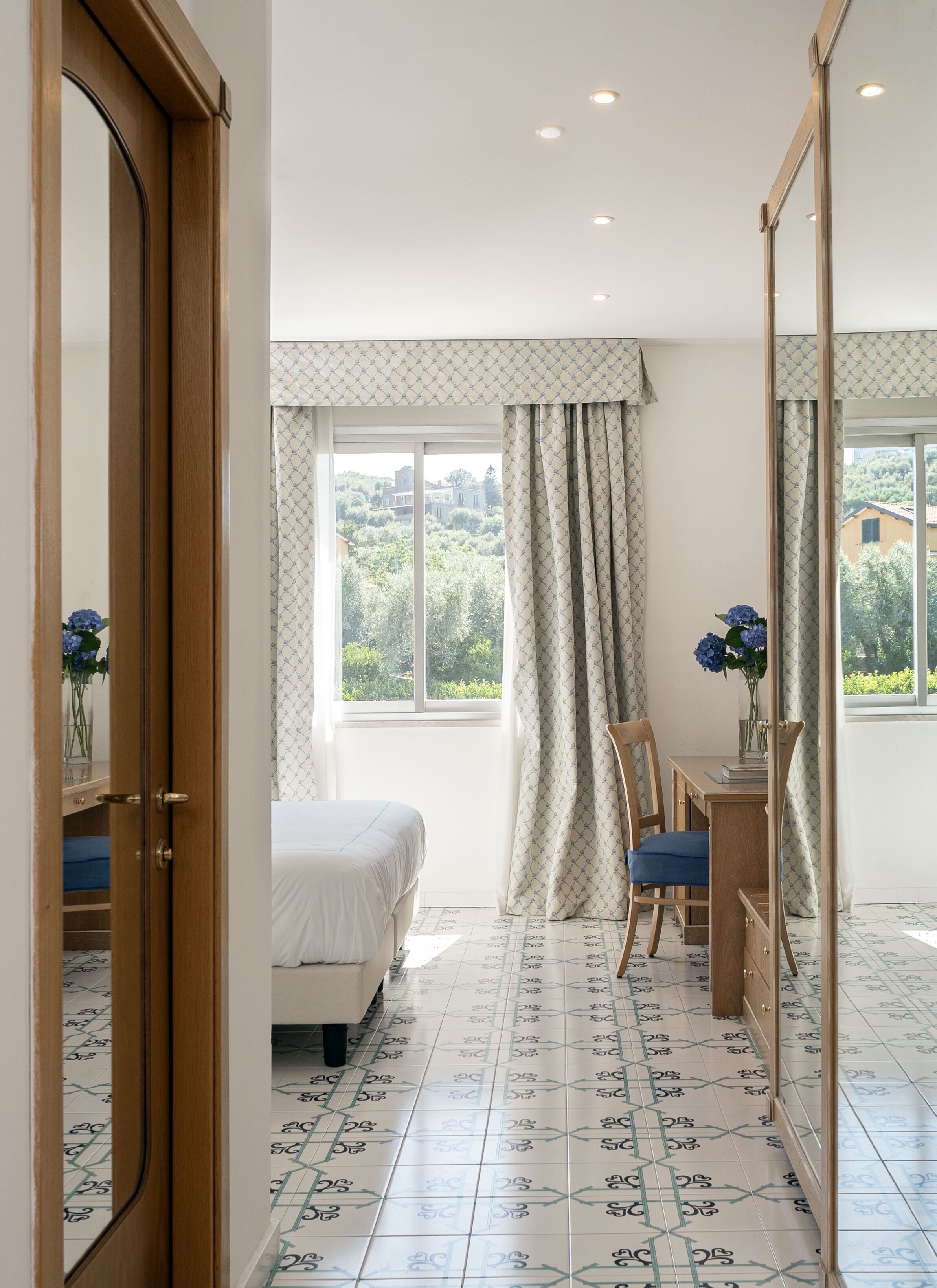 A bedroom with a bed, a desk, a chair, and a mirror.