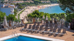 Zona de piscina con sillones de descanso y vista a una playa y al océano.