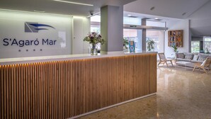 Un área de recepción con diseño moderno, que incluye un mostrador de recepción, una zona de estar con sofá y sillas, y un amplio ventanal que proporciona luz natural.