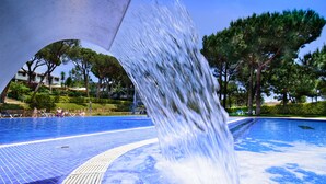 A swimming pool with a waterfall feature, surrounded by trees and a clear sky.