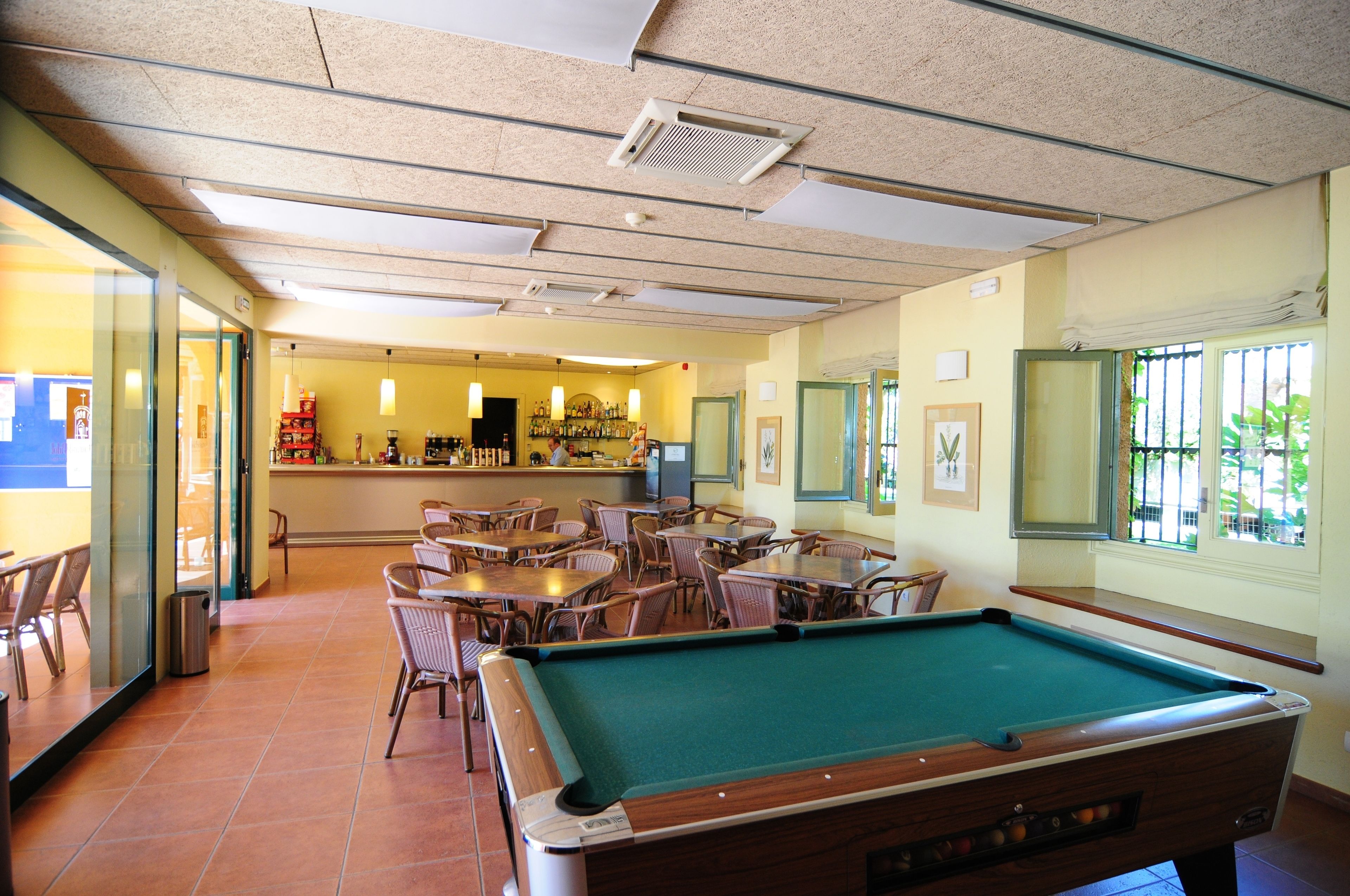 A pool table in a room with chairs and tables, a bar area, and a window with a view.