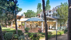 A covered outdoor dining area with tables and chairs, surrounded by trees and a garden path.