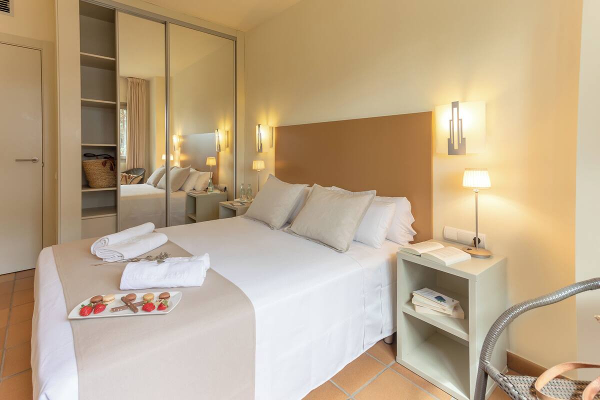 Ein Hotelzimmer mit einem großen Bett, einem Nachttisch mit Lampe, einem Sessel, einem Kleiderschrank und einer Schale Erdbeeren und Schokolade.