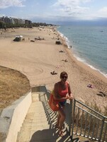 Una escalera que desciende hacia una playa, con vista despejada al océano y algunas personas a lo lejos.
