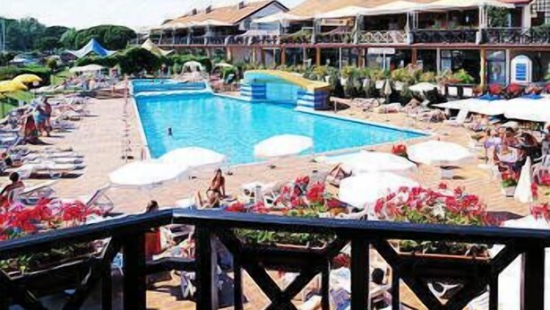 Zona de piscina con sillones de descanso y sombrillas, rodeada de edificios con balcones.