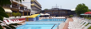 A swimming pool with lounge chairs and umbrellas, surrounded by buildings with balconies and a restaurant. - Hotel Marina Uno (Lignano Sabbiadoro)